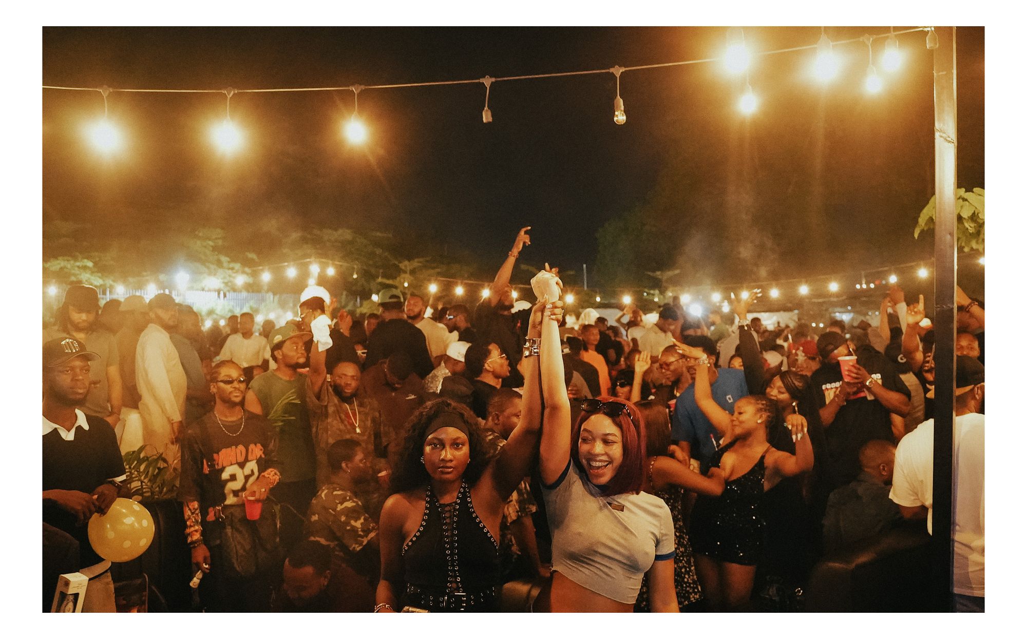 Two women raising hands together in the crowd at Romie's Block